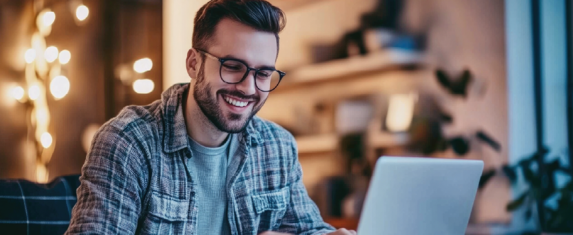 Homem de óculos e camisa xadrez sorrindo trabalhando em laptop