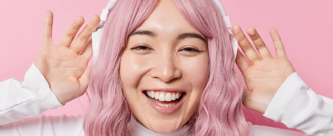 Garota coreana de cabelo rosa, sorrindo, usando um fone de ouvido branco.