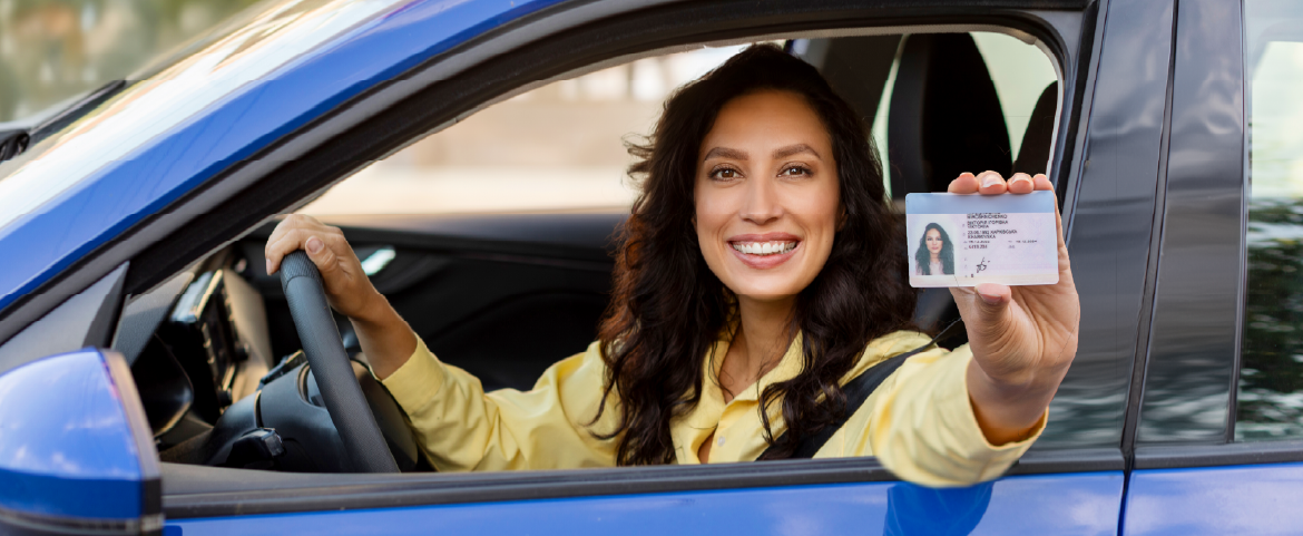 Mulher dentro de carro azul, sorrindo e mostrando documento.