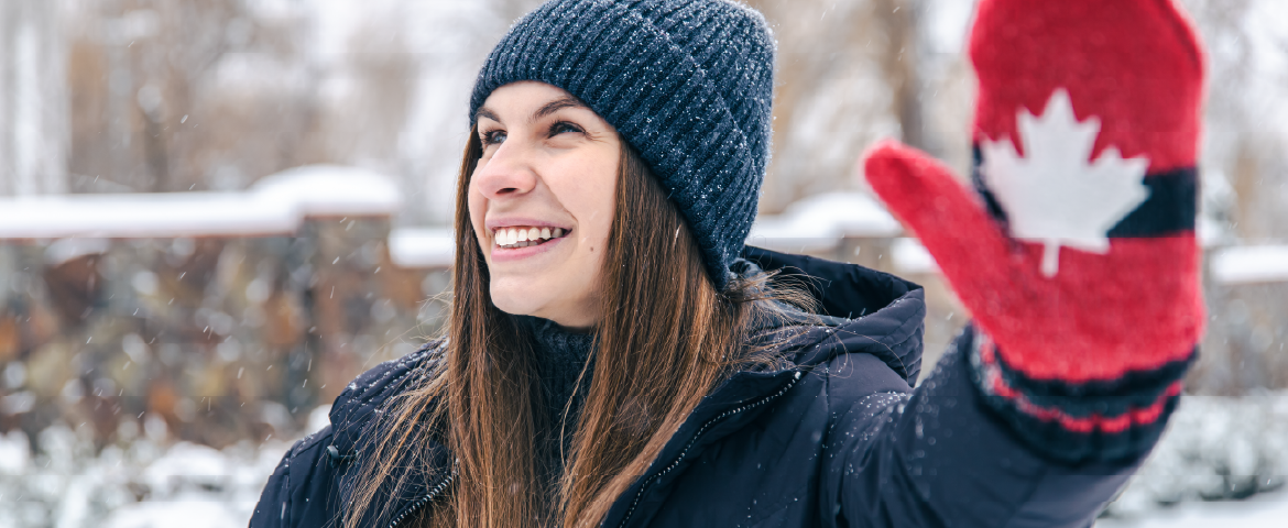 Mulher sorridente com roupa de inverno, com luva de lã com tema do Canadá.
