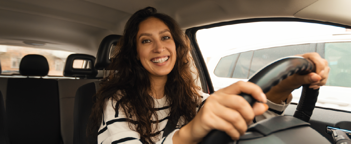 Mulher dentro do carro com a mão ao volante e sorrindo