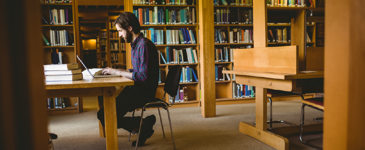 Homem estudando em biblioteca. Homem com laptop estudando em biblioteca.
