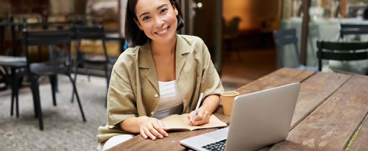 Mulher oriental trabalhando com laptop e tomando notas em um café europeu. Mulher oriental estudando com laptop e tomando notas em um café europeu.