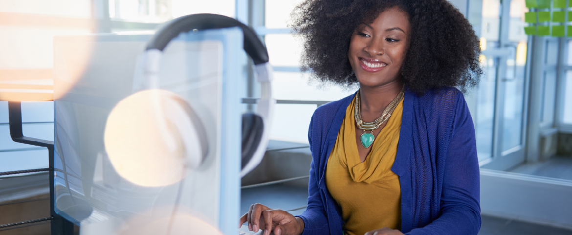 Mulher sorrindo e olhando para a tela de um computador.