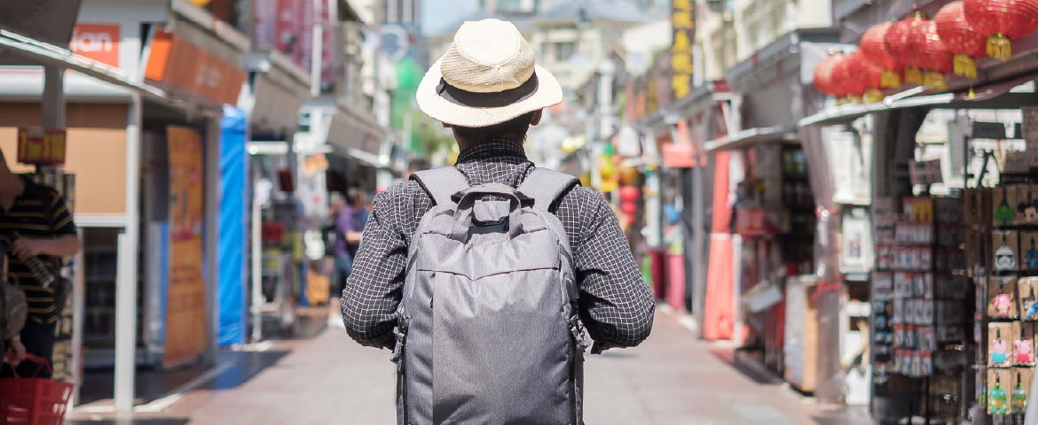 Homem usando chapéu e mochila nas costas visitando um bairro oriental.