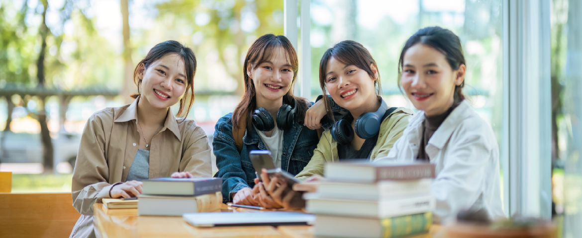 Grupo de estudantes orientais, felizes estudando na biblioteca com alguns livros sobre a mesa.
