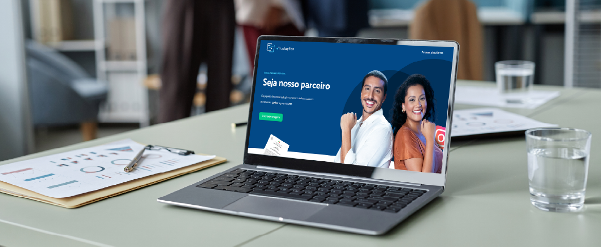 Laptop sobre a mesa com algumas planilhas e a tela exibindo a home do Programa Partners da eTraduções.