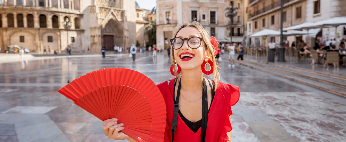 Mulher espanhola em ponto turístico sorrindo com um leque vermelho na mão.